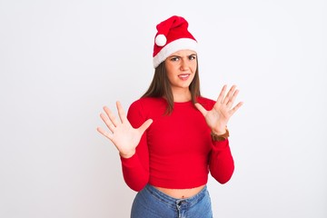 Obraz na płótnie Canvas Young beautiful girl wearing Christmas Santa hat standing over isolated white background afraid and terrified with fear expression stop gesture with hands, shouting in shock. Panic concept.