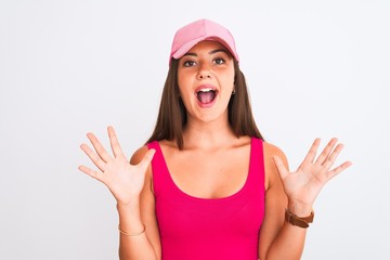 Obraz na płótnie Canvas Young beautiful girl wearing pink casual t-shirt and cap over isolated white background celebrating crazy and amazed for success with arms raised and open eyes screaming excited. Winner concept