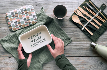 Creative flat lay, zero waste lunch concept with set of reusable wooden cutlery, lunch box, drinking bottle and reusable coffee cup. Sustainable lifestyle top view, flat layout with text on wood.