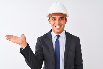 Young handsome architect man wearing suit and helmet over isolated white background smiling cheerful presenting and pointing with palm of hand looking at the camera.
