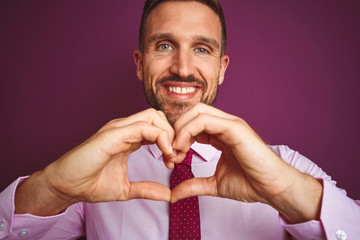 Close up of business man wearing elegant shirt and tie over purple isolated background smiling in love showing heart symbol and shape with hands. Romantic concept.