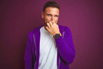 Young fitness man wearing casual sports sweatshirt over purple isolated background smelling...