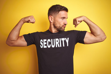 Young safeguard man wearing security uniform over yellow isolated background showing arms muscles...