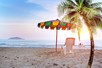 Fototapeta na wymiar White beach chair and umbrella on tropical beach with orange sky