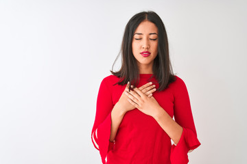 Young beautiful chinese woman wearing red dress standing over isolated white background smiling with hands on chest with closed eyes and grateful gesture on face. Health concept.