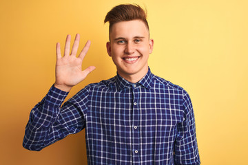 Fototapeta premium Young handsome man wearing casual shirt standing over isolated yellow background showing and pointing up with fingers number five while smiling confident and happy.