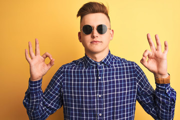 Naklejka premium Young handsome man wearing casual shirt and sunglasses over isolated yellow background relax and smiling with eyes closed doing meditation gesture with fingers. Yoga concept.