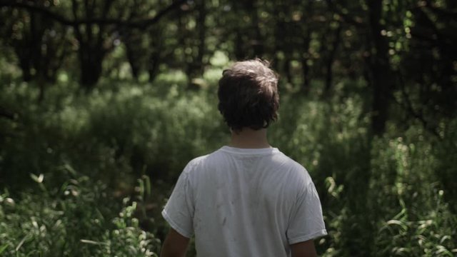 Teen boy walks through forest trees