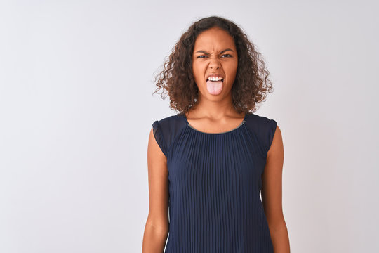 Young brazilian woman wearing blue dress standing over isolated white background sticking tongue out happy with funny expression. Emotion concept.