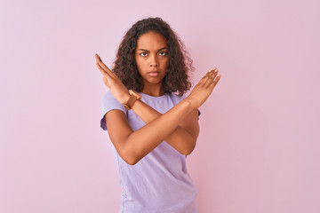 Young brazilian woman wearing t-shirt standing over isolated pink background Rejection expression crossing arms doing negative sign, angry face