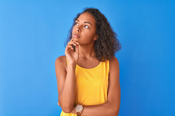 Young brazilian woman wearing yellow t-shirt standing over isolated blue background with hand on...