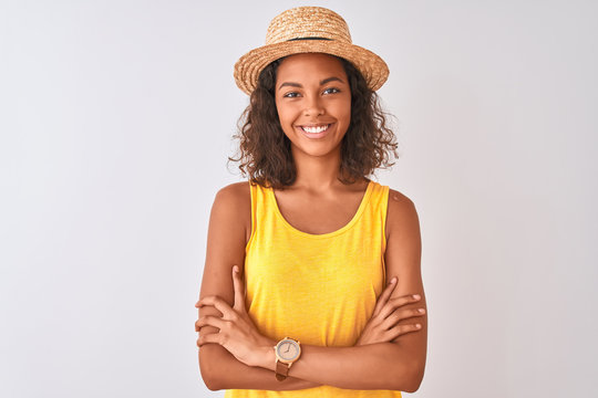 Young brazilian woman wearing yellow t-shirt and summer hat over isolated white background happy face smiling with crossed arms looking at the camera. Positive person.