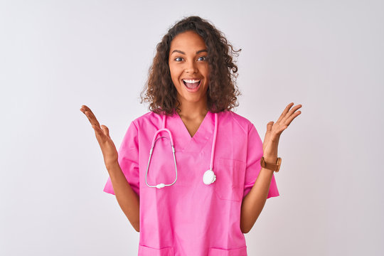 Young brazilian nurse woman wearing stethoscope standing over isolated white background celebrating crazy and amazed for success with arms raised and open eyes screaming excited. Winner concept