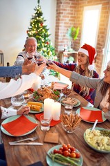 Beautiful family wearing santa claus hat meeting smiling happy and confident. Eating roasted turkey toasting with cup of wine celebrating Christmas at home