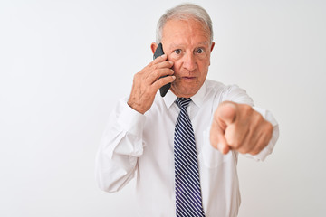 Senior grey-haired businessman talking on the smartphone over isolated white background pointing with finger to the camera and to you, hand sign, positive and confident gesture from the front