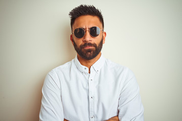 Handsome indian buinessman wearing shirt and sunglasses over isolated white background skeptic and...