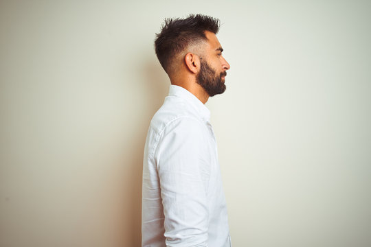 Young indian man wearing elegant shirt standing over isolated white background looking to side, relax profile pose with natural face with confident smile.