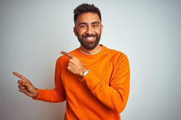 Young indian man wearing orange sweater over isolated white background smiling and looking at the...