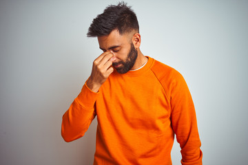 Young indian man wearing orange sweater over isolated white background tired rubbing nose and eyes feeling fatigue and headache. Stress and frustration concept.