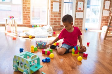 Adorable toddler playing with building blocks around lots of toys at kindergarten