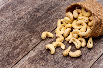 Cashew nut in sack cloth on wooden table background. 