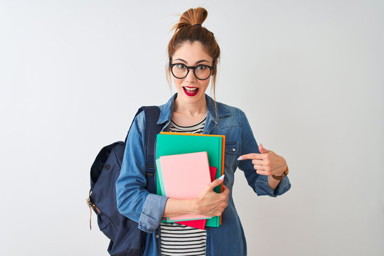 Redhead student woman wearing backpack holding books over isolated white background very happy pointing with hand and finger