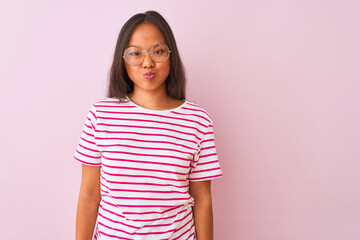 Fototapeta premium Young chinese woman wearing striped t-shirt and glasses over isolated pink background puffing cheeks with funny face. Mouth inflated with air, crazy expression.