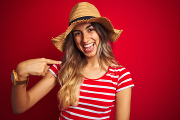 Young beautiful woman wearing summer hat over red isolated background with surprise face pointing finger to himself