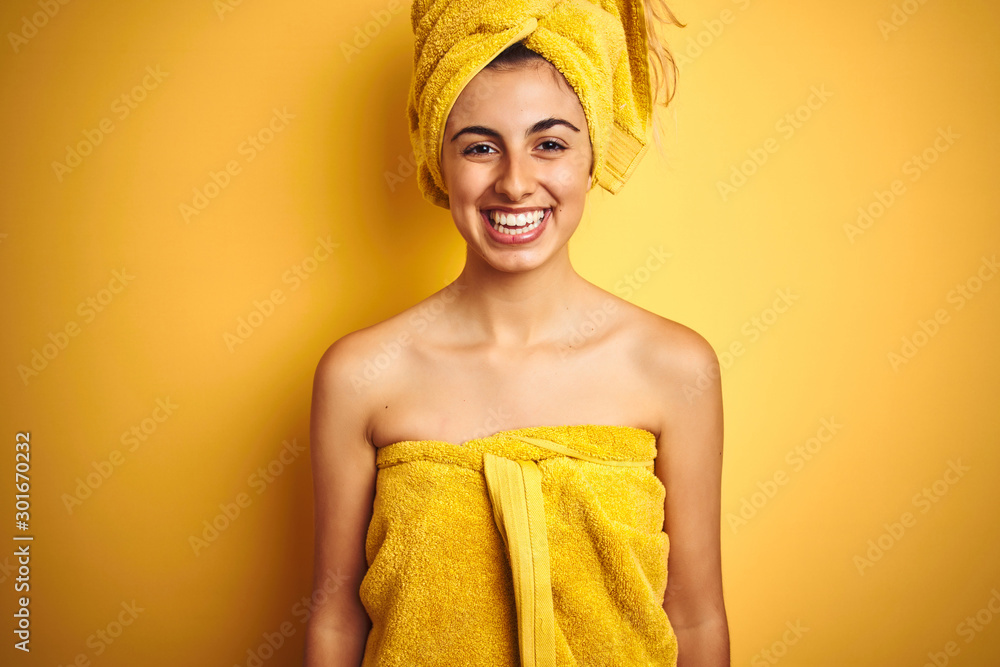 Poster young beautiful woman wearing a shower towel after bath over yellow isolated background with a happy