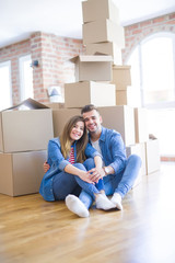 Young beautiful couple in love moving to new home, sitting on the floor very happy and cheerful for new apartment around cardboard boxes