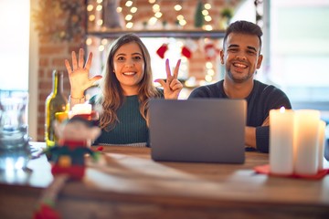 Young beautiful couple sitting using laptop around christmas decoration at home showing and pointing up with fingers number eight while smiling confident and happy.