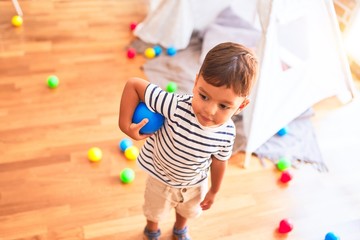 Beautiful toddler boy playing with colored small balls at kindergarten