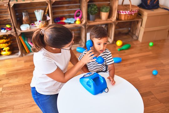 Beautiful teacher and toddler boy playing with vintage blue phone at kindergarten