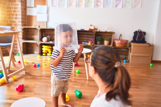 Beautiful teacher and toddler boy playing with plastic basket at kindergarten