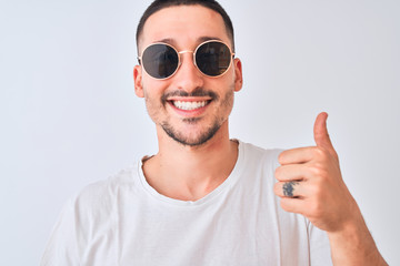 Young handsome man wearing sunglasses and casual t-shirt over isolated background happy with big smile doing ok sign, thumb up with fingers, excellent sign