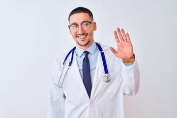 Young doctor man wearing stethoscope over isolated background Waiving saying hello happy and...