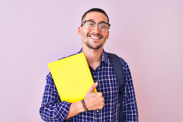 Young handsome student man holding a book over isolated background with a happy face standing and...