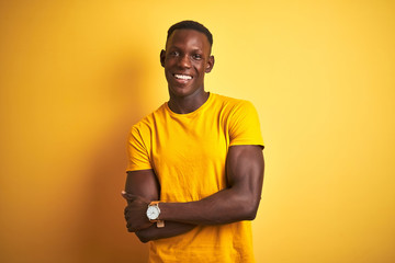 Young african american man wearing casual t-shirt standing over isolated yellow background happy face smiling with crossed arms looking at the camera. Positive person.