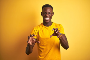 Young african american man wearing casual t-shirt standing over isolated yellow background smiling funny doing claw gesture as cat, aggressive and sexy expression