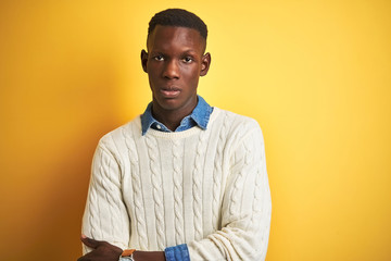 Obraz premium African american man wearing denim shirt and white sweater over isolated yellow background skeptic and nervous, disapproving expression on face with crossed arms. Negative person.