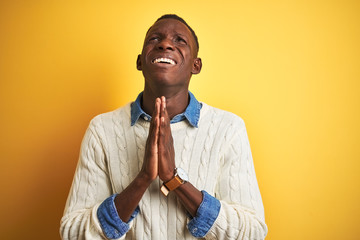 African american man wearing denim shirt and white sweater over isolated yellow background begging...