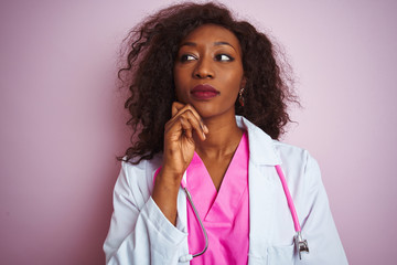 African american doctor woman wearing stethoscope over isolated pink background with hand on chin thinking about question, pensive expression. Smiling with thoughtful face. Doubt concept.