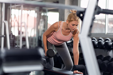 Strong woman doing exercises with dumbbells in gym