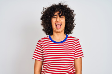 Fototapeta na wymiar Young arab woman with curly hair wearing striped t-shirt over isolated white background sticking tongue out happy with funny expression. Emotion concept.