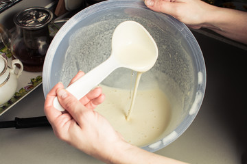 Girls hand is picking up mixture from large cup for baking pancakes.