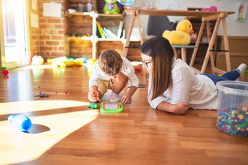 Fototapeta premium Beautiful teacher and toddler drawing using digital board around lots of toys at kindergarten