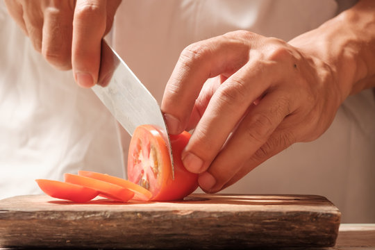 Chef cut tomato on cutting board with knife