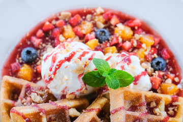 Close up of Sweet waffles with strawberries sauce vanilla ice cream and fresh fruit green mint leaves on white plate at cafe restaurant ,holiday summertime.