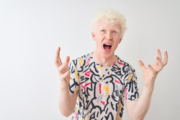 Young albino blond man wearing colorful t-shirt standing over isolated white background crazy and mad shouting and yelling with aggressive expression and arms raised. Frustration concept.