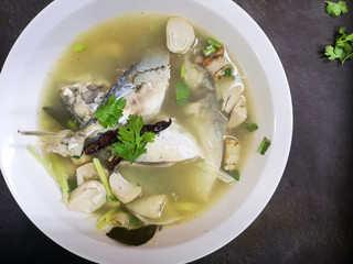 Top view of Spicy Mackerel Soup (Tom Yum Pla Tu)Thai traditional local food in white bowl on dark background, spicy hot & sour soup with herbs.